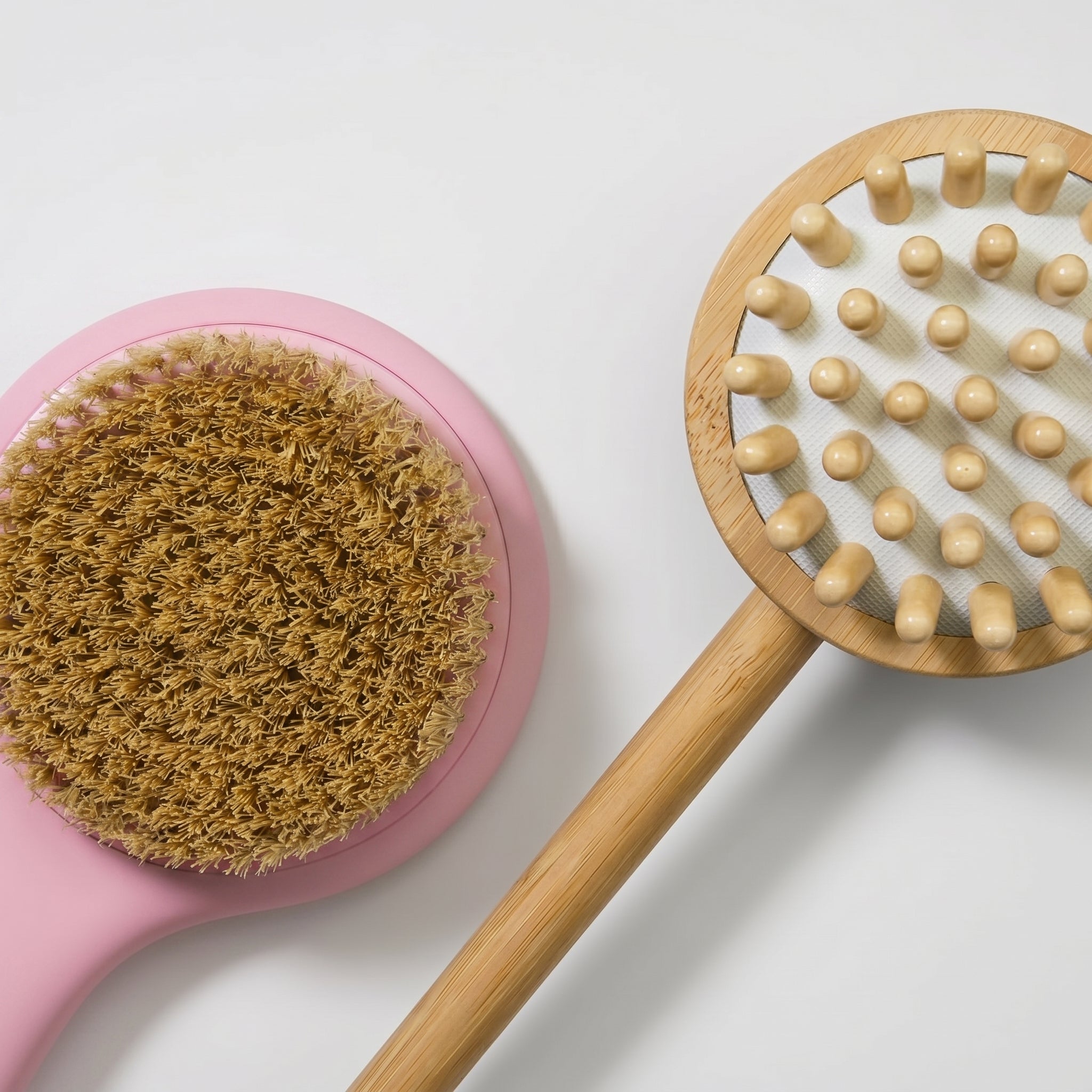 Pink body brush with brown bristles and wooden massage brush on a white background